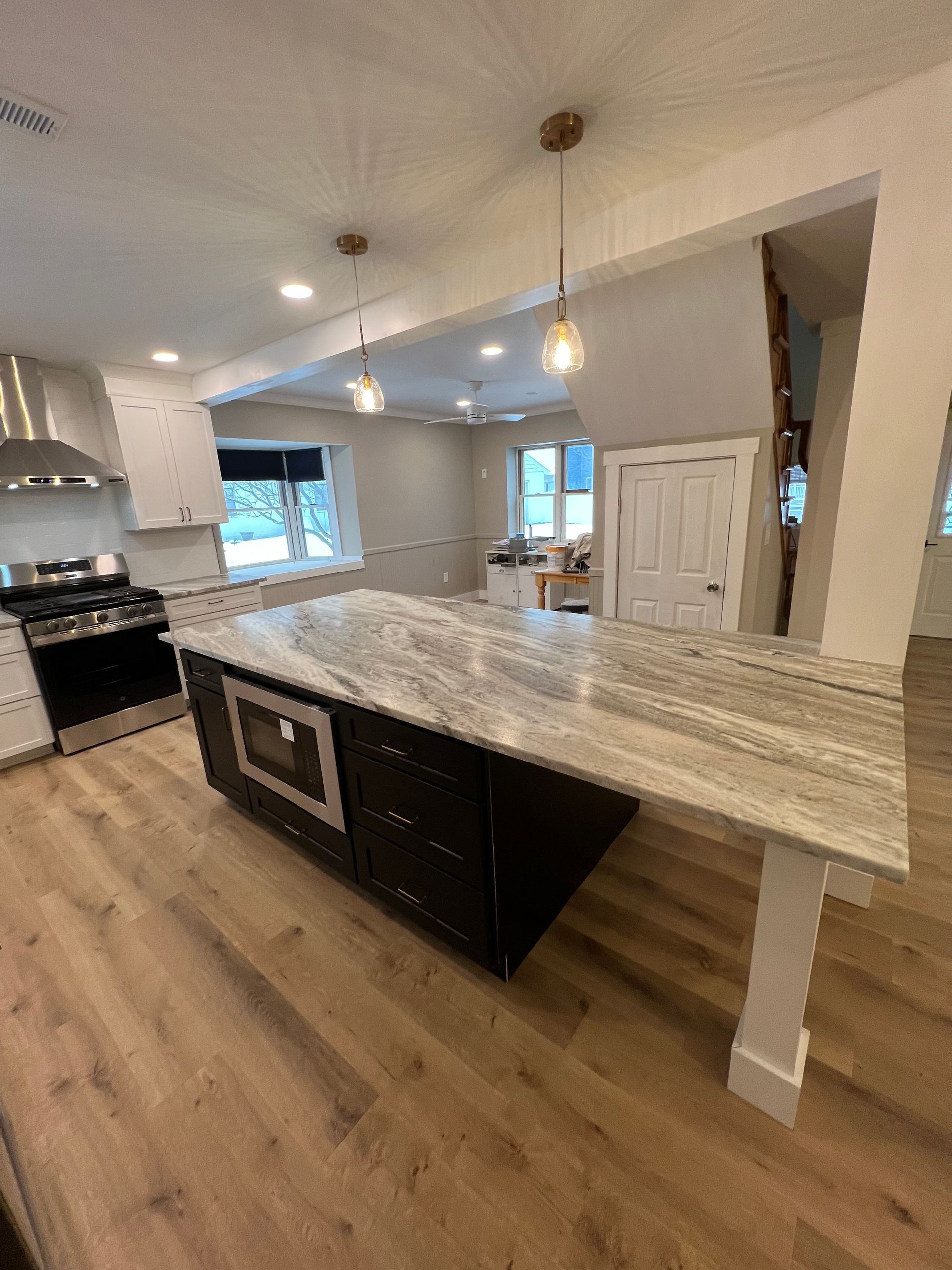 Modern kitchen with a dark island and a light granite countertop. Hardwood floors and pendant lights.