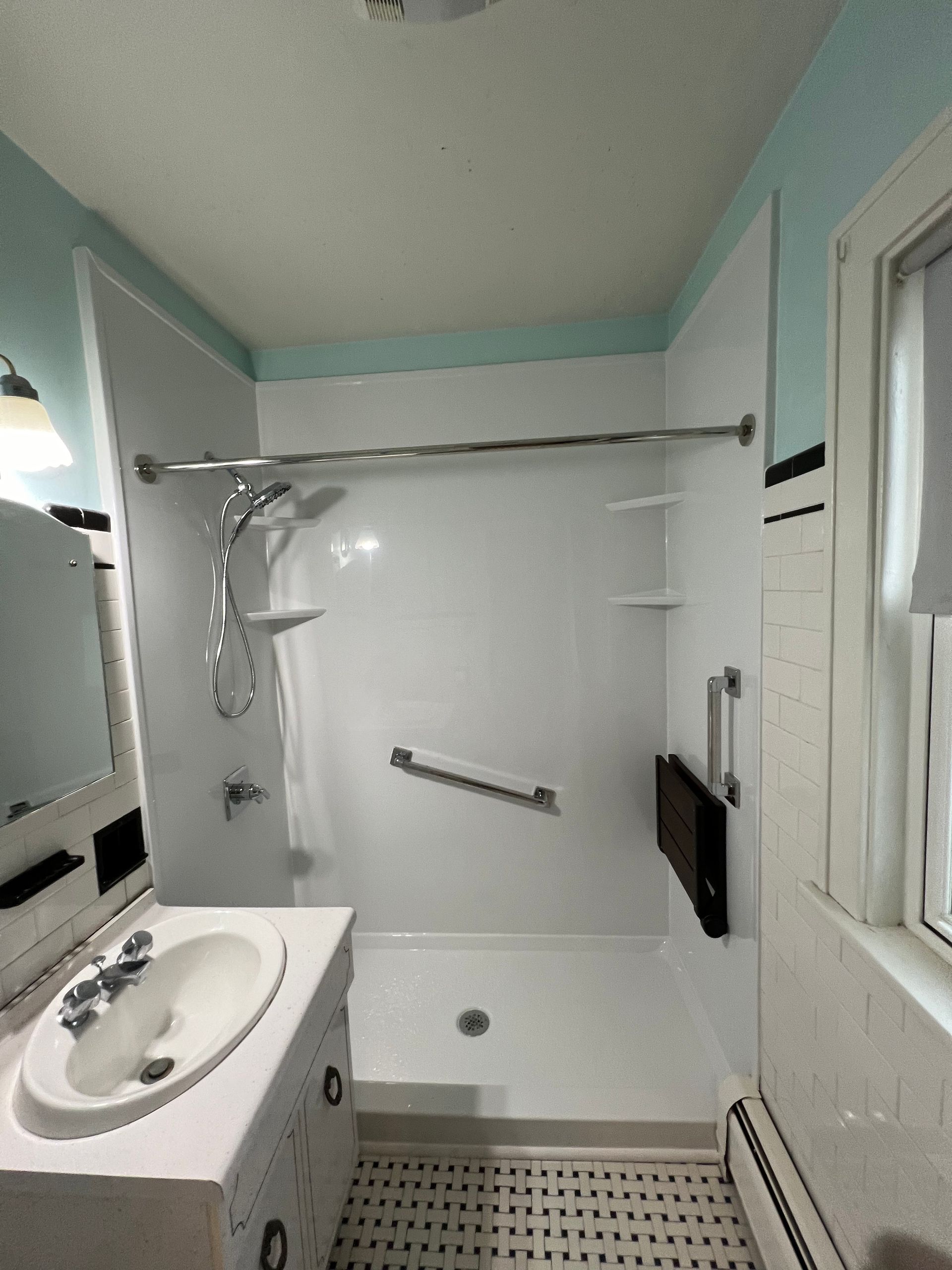 Small bathroom with white walk-in shower, sink vanity, and black-and-white tile floor.