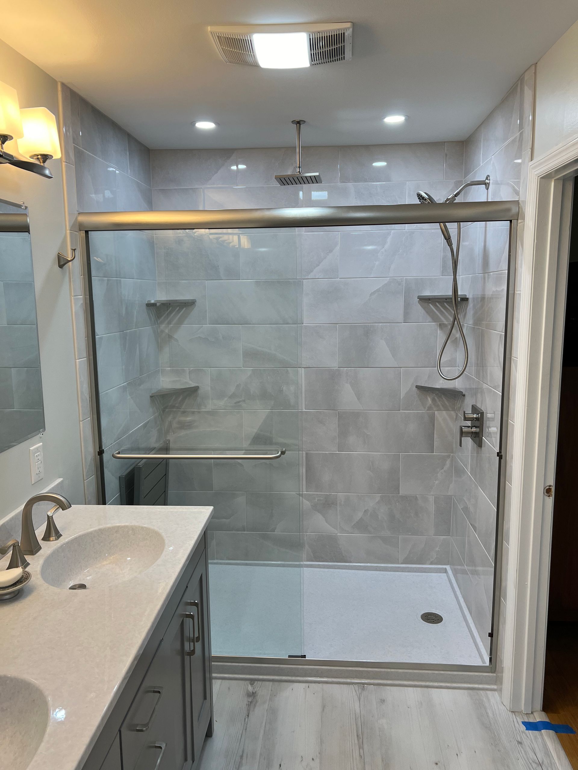 A modern bathroom featuring a grey vanity, a glass-enclosed shower with light-colored tile walls, and overhead lighting.