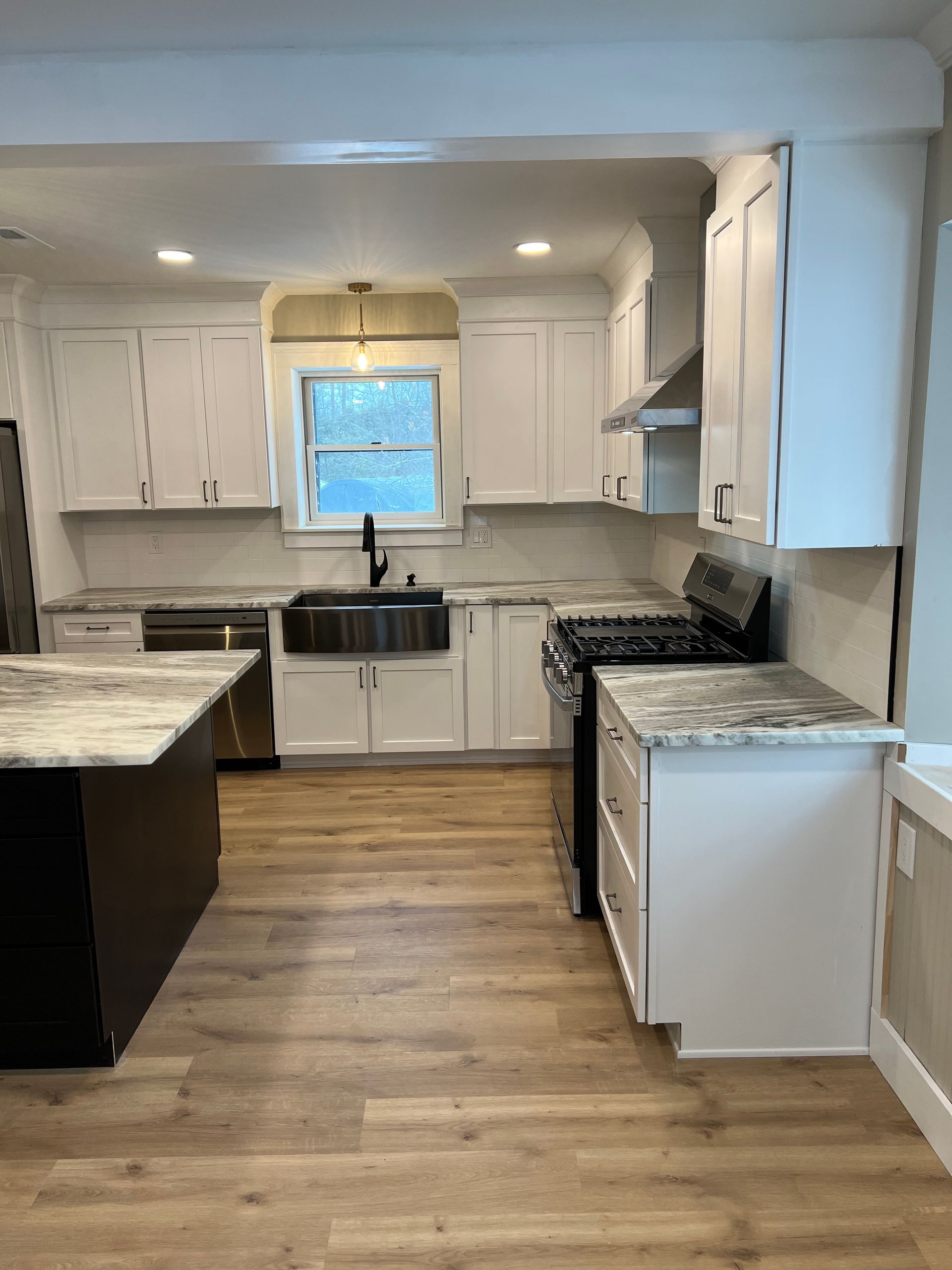 Modern white kitchen with marble-look counters, black farmhouse sink, and wood floors.