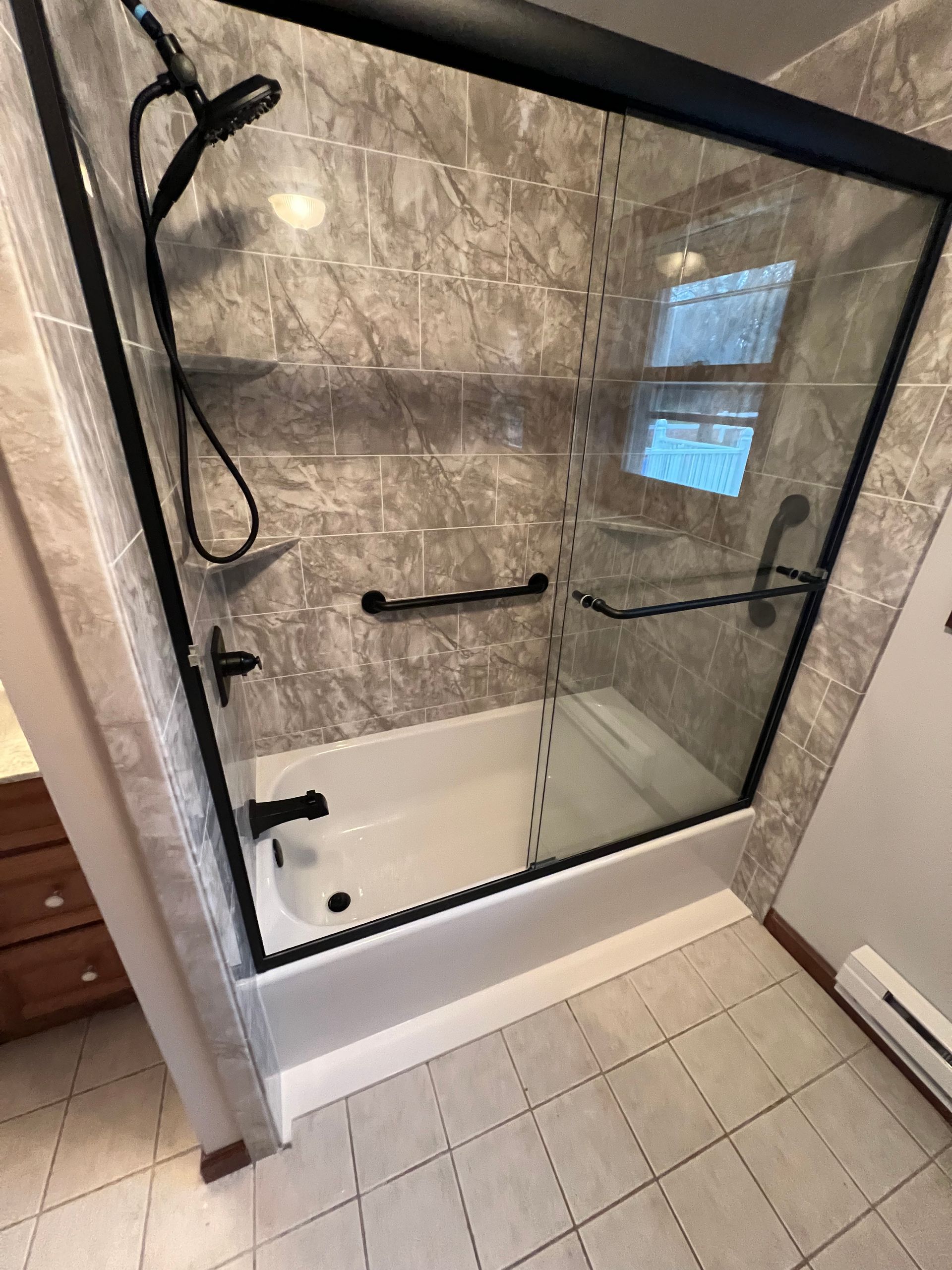A bathroom with a bathtub and a shower with a black frame.