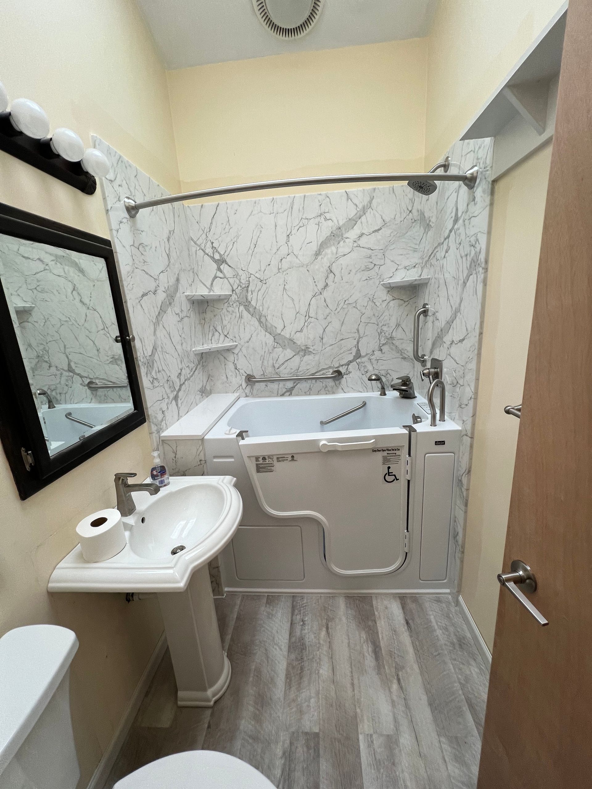 A bathroom with a walk in tub , sink , toilet and mirror.
