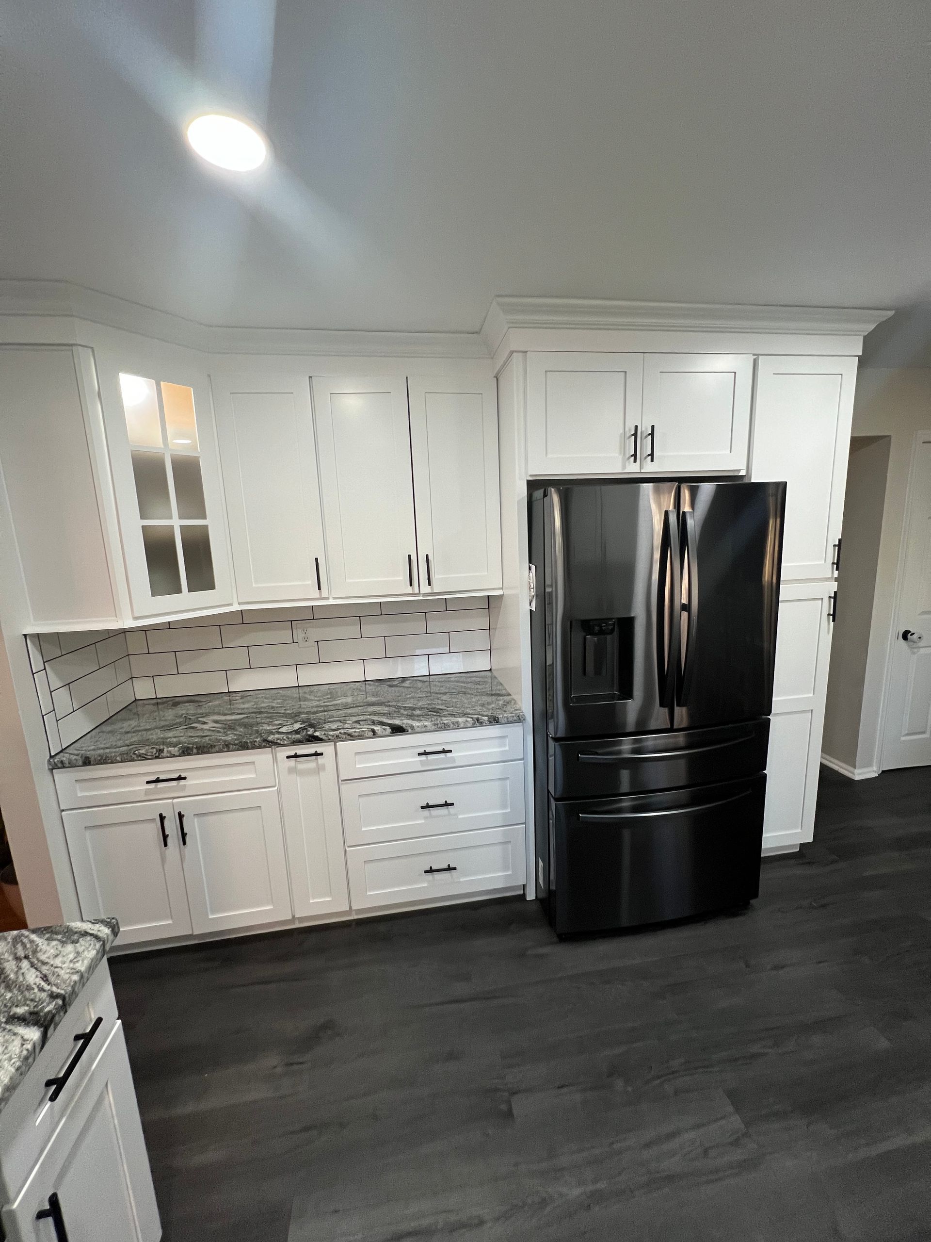 A kitchen with white cabinets and a black refrigerator.
