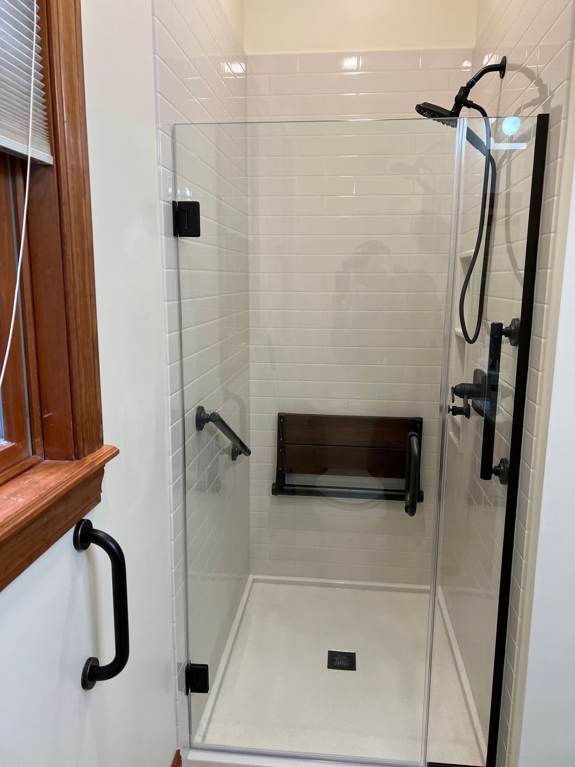 A bathroom with a walk in shower with a glass door and a window.