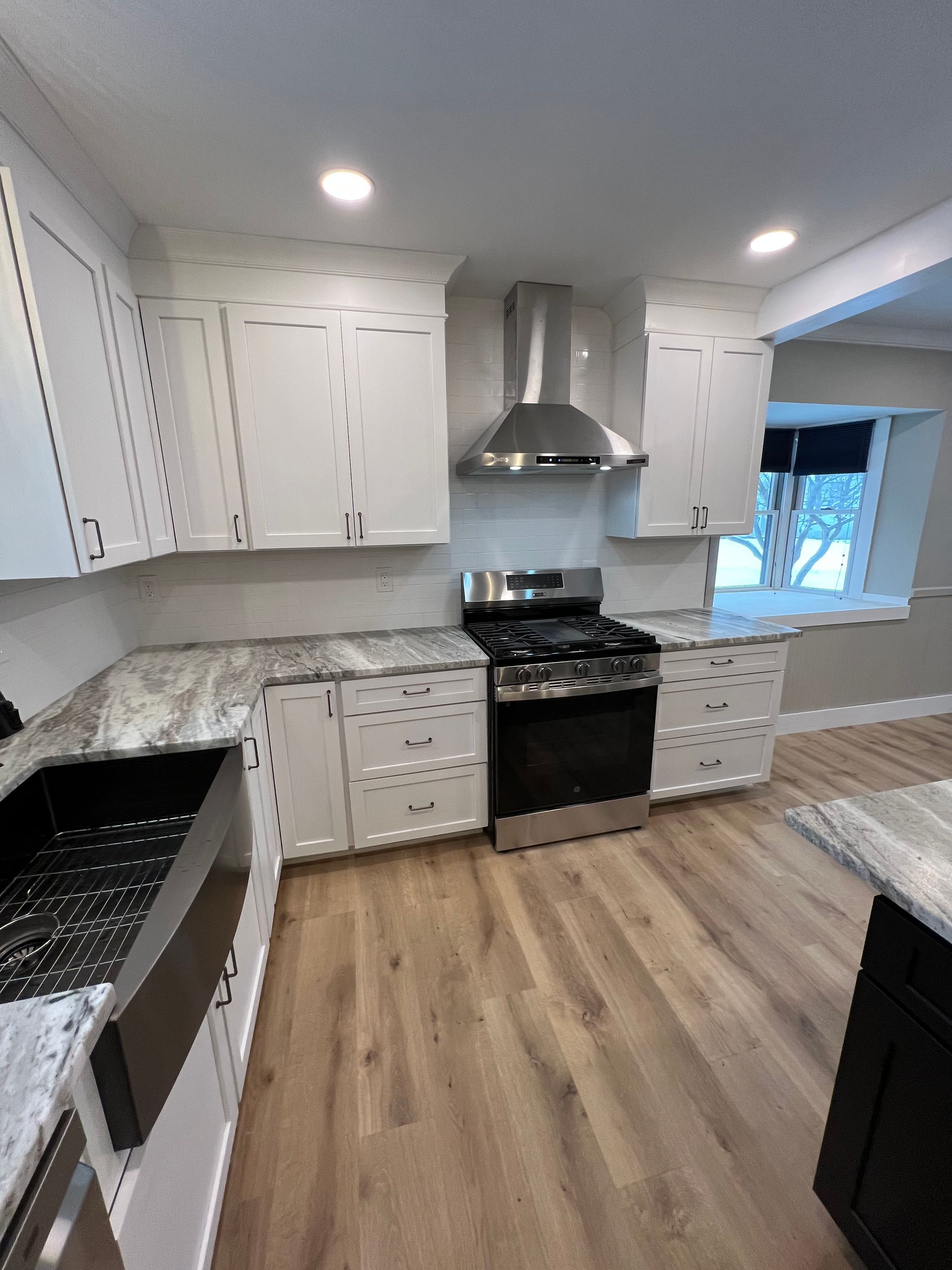 A kitchen with white cabinets , a stove , a sink , and a window.