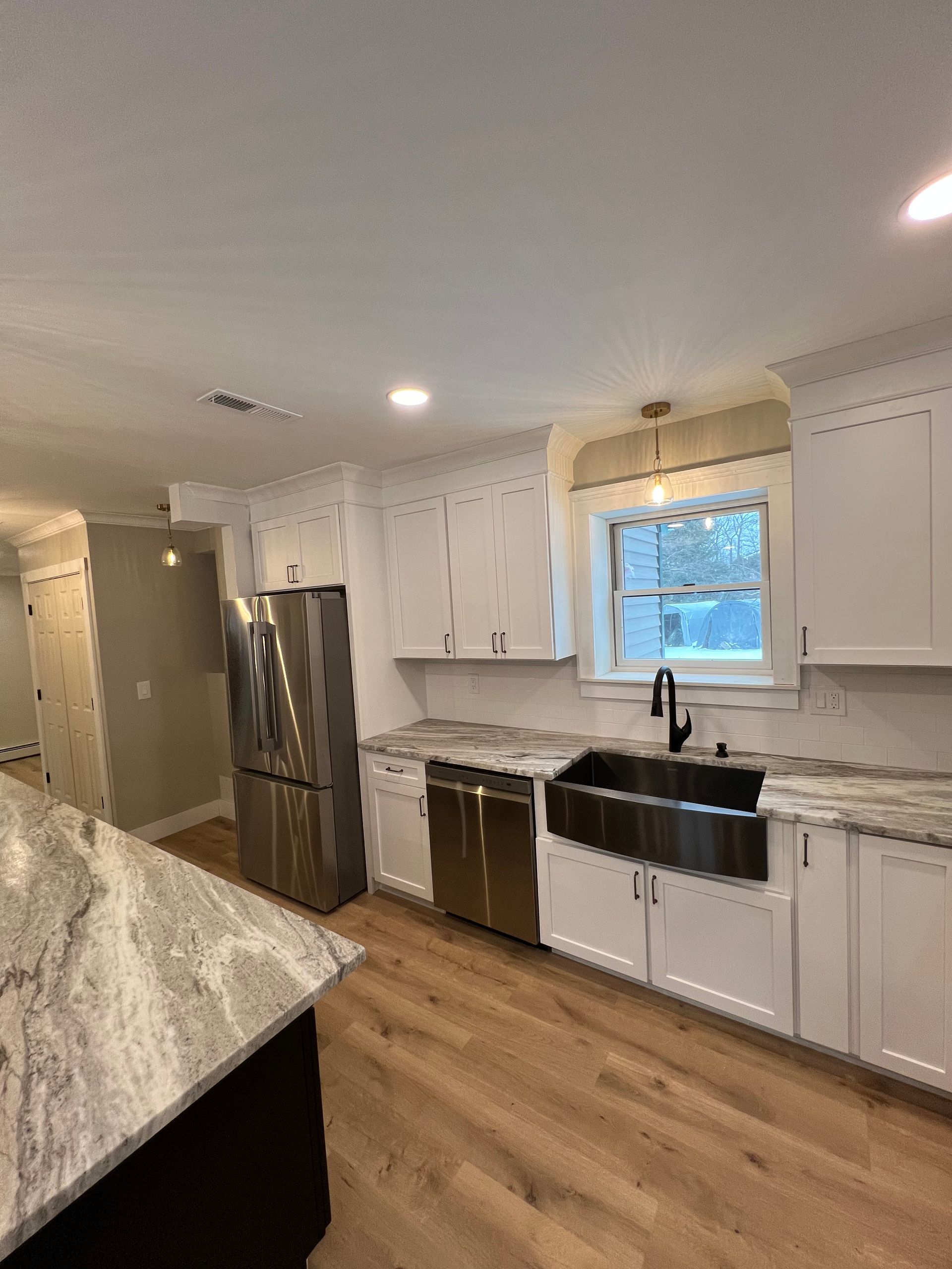 A kitchen with white cabinets , stainless steel appliances , a sink and a refrigerator.