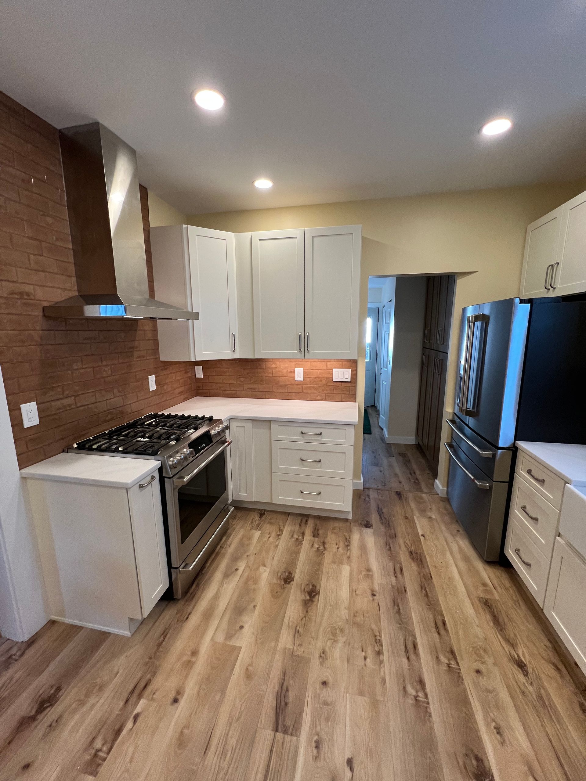 A kitchen with hardwood floors , stainless steel appliances , and white cabinets.