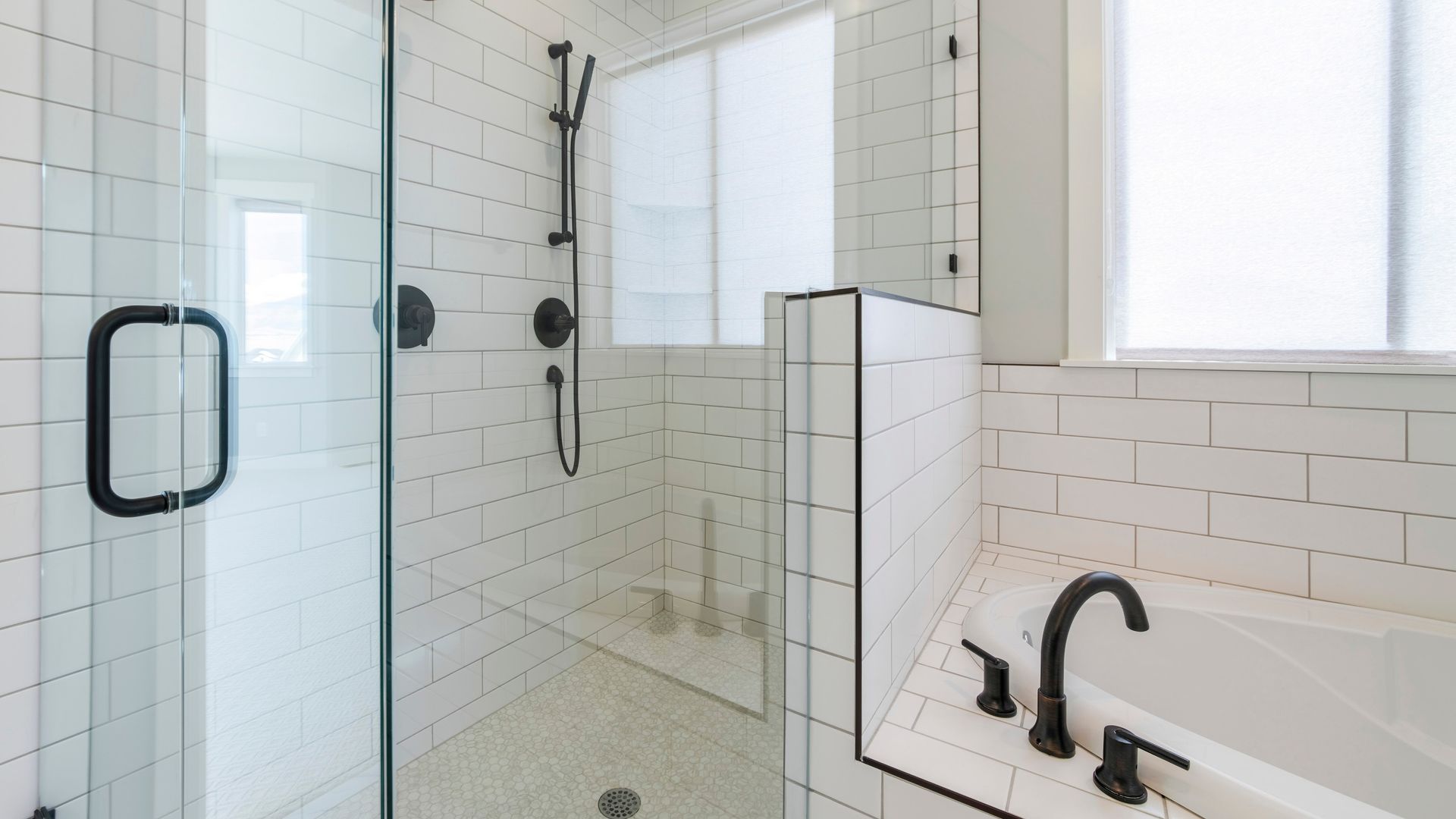 A bathroom with white tiles , a tub , a shower and a window.