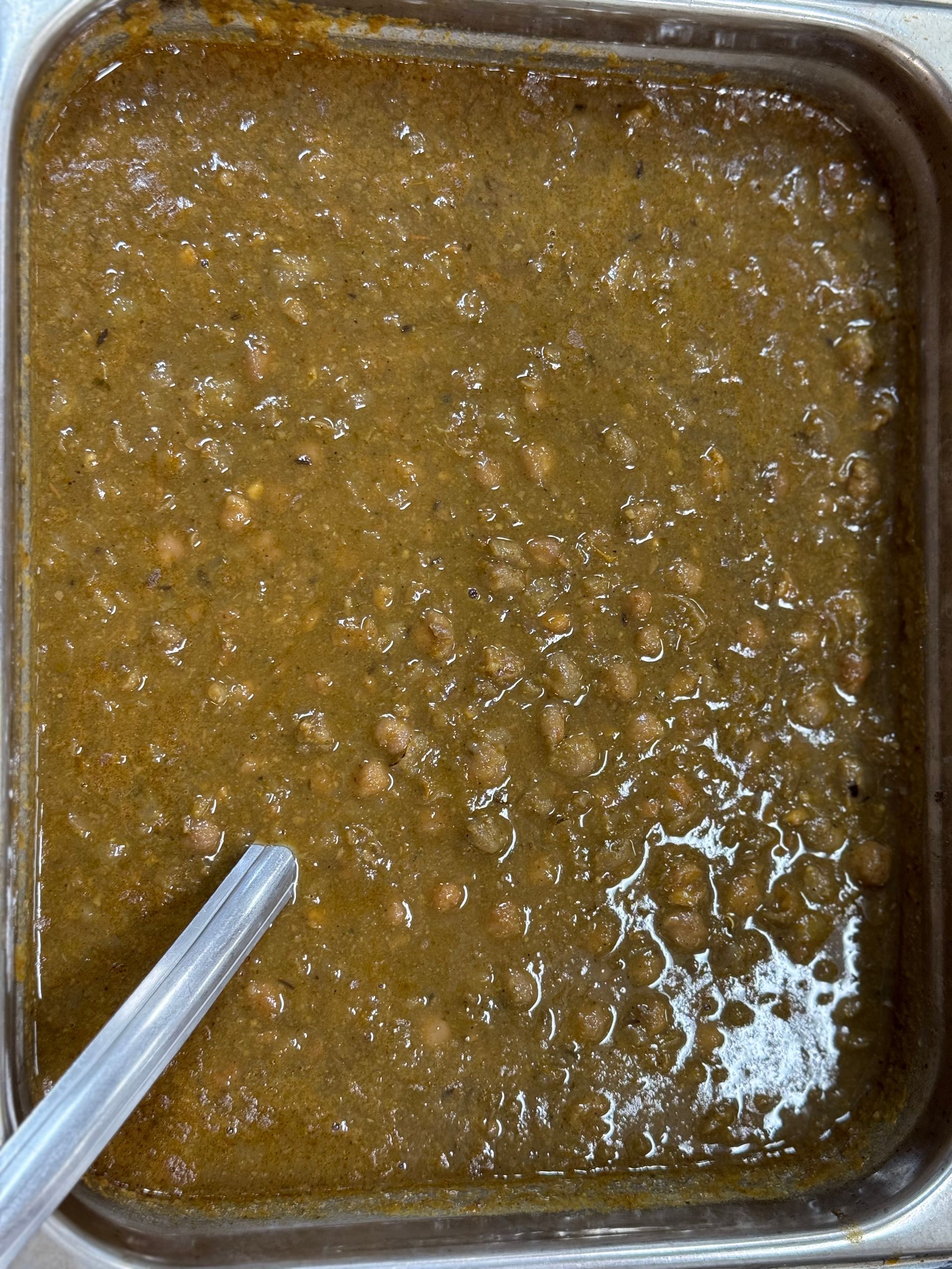 Close-up of a pan of dark brown chickpea curry with a serving spoon.