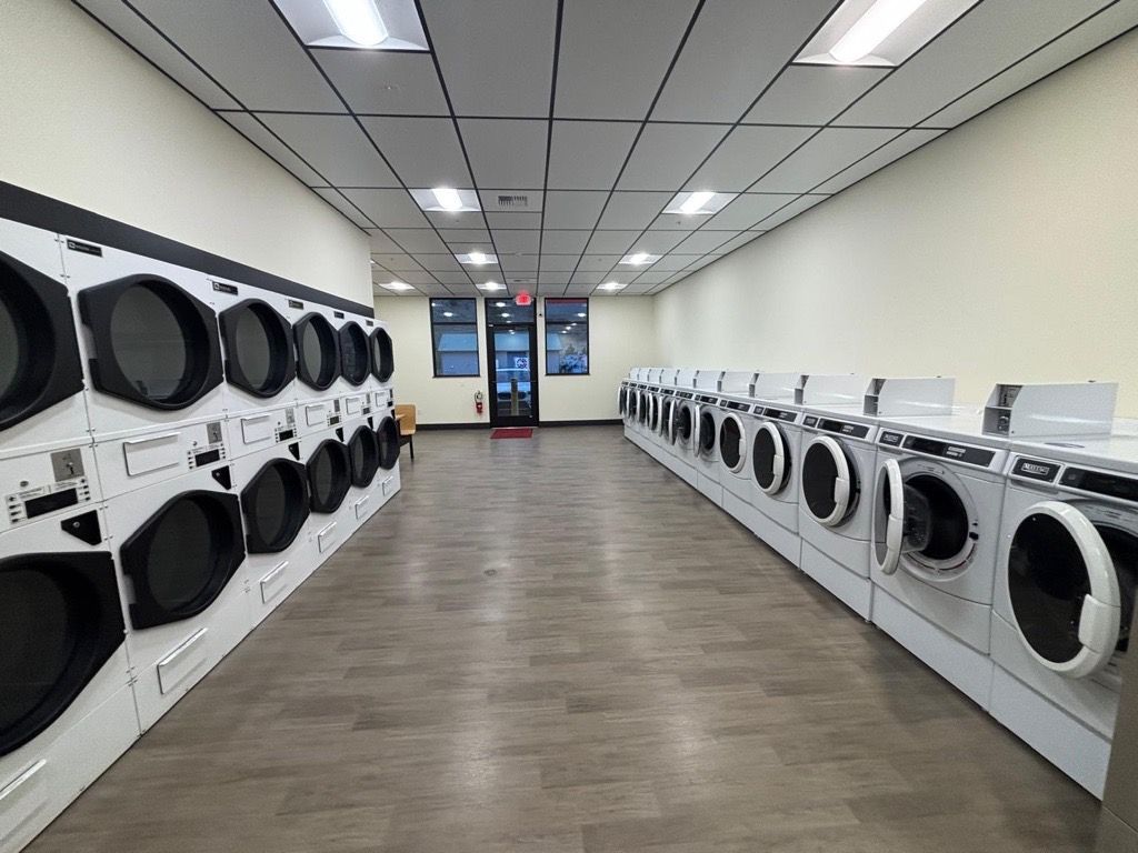 A laundromat with rows of washing machines. The floor is brown and the walls are light colored.
