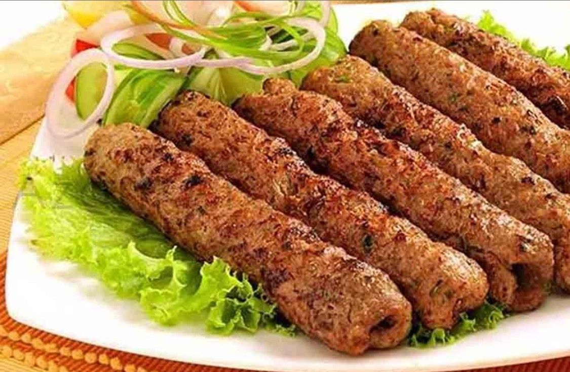 Grilled kebabs on a plate with lettuce, onion, cucumber, and lemon.