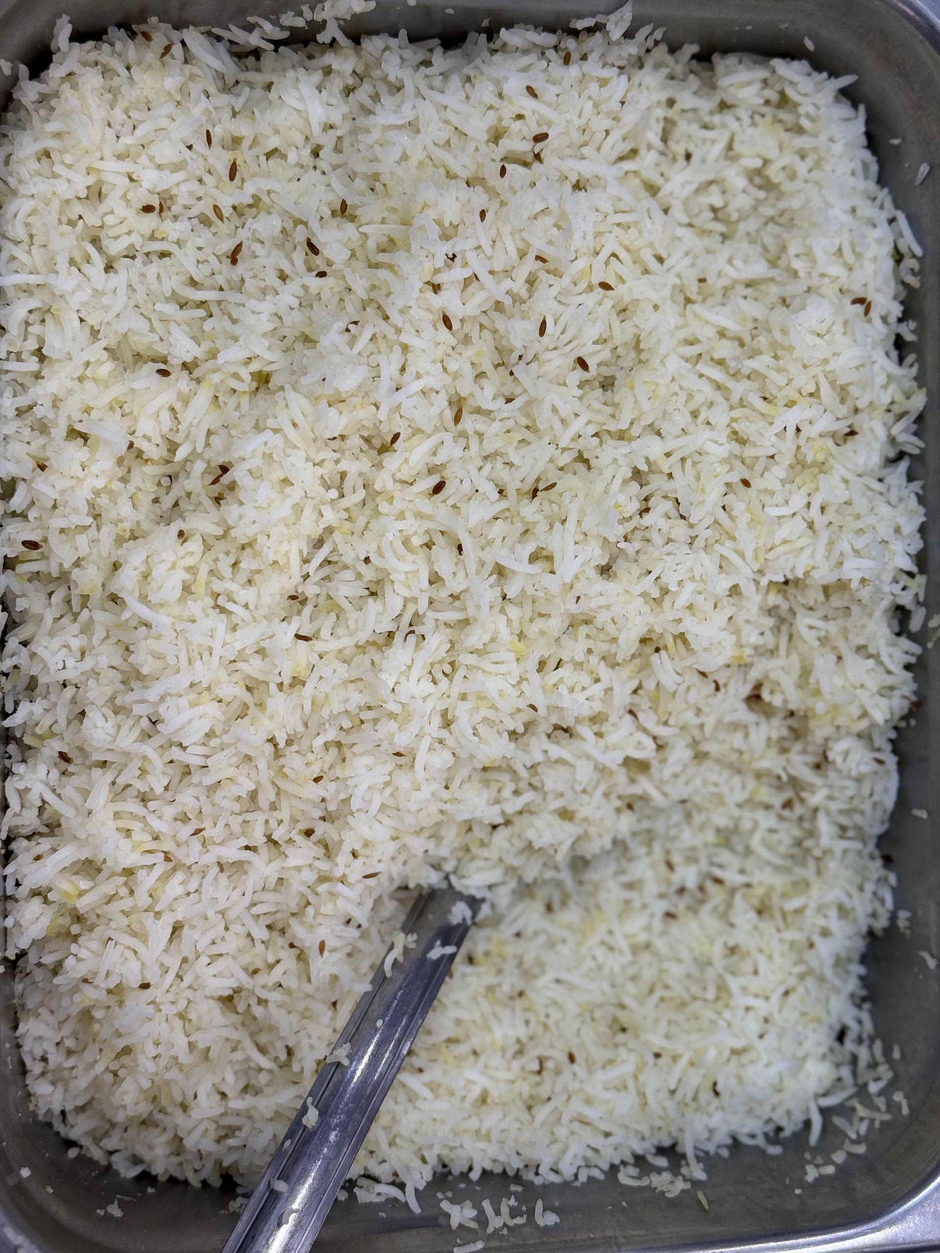 White rice in a rectangular metal container, with a serving utensil.