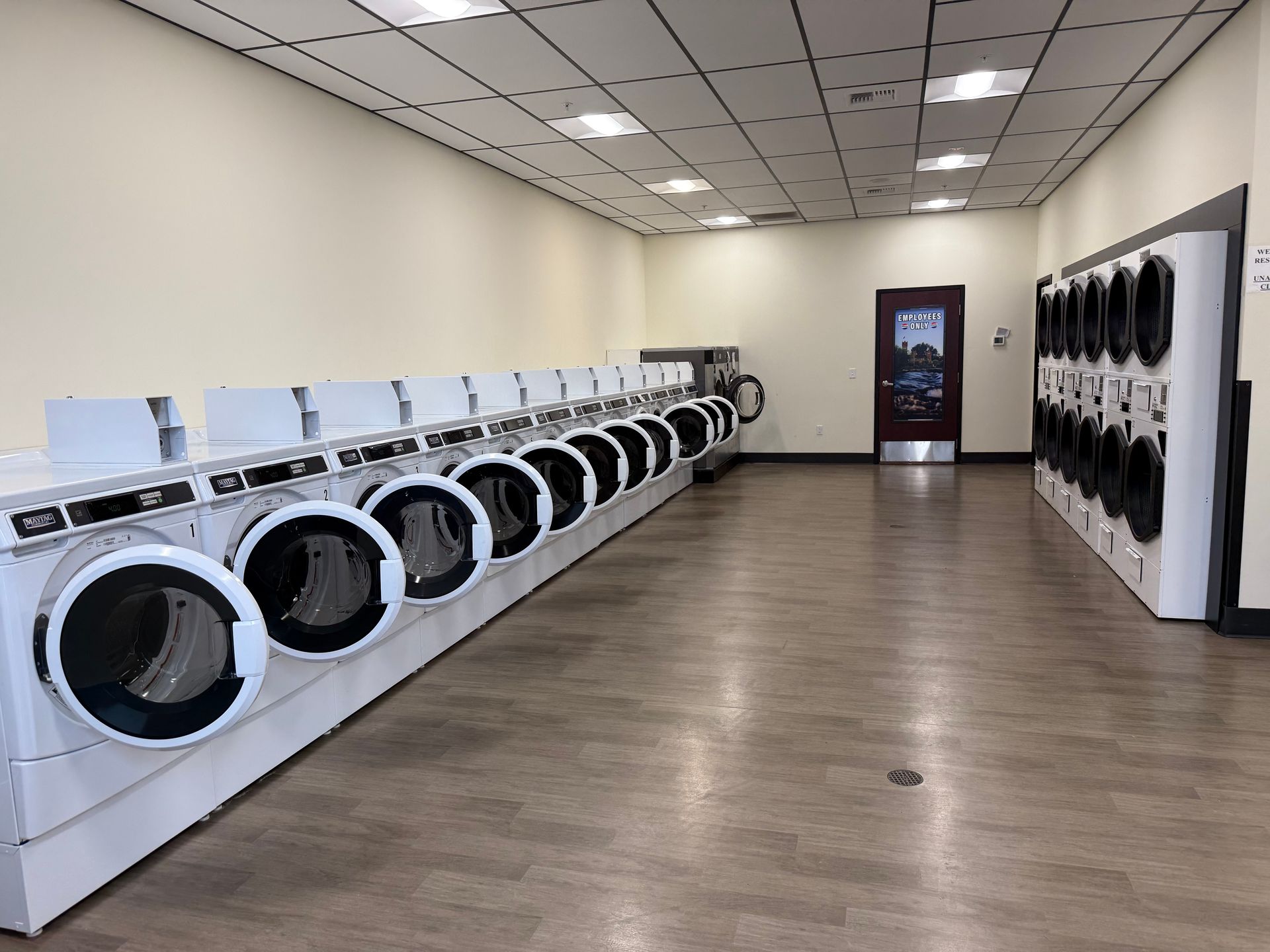 A laundromat with rows of washing machines. The floor is brown and the walls are light colored.