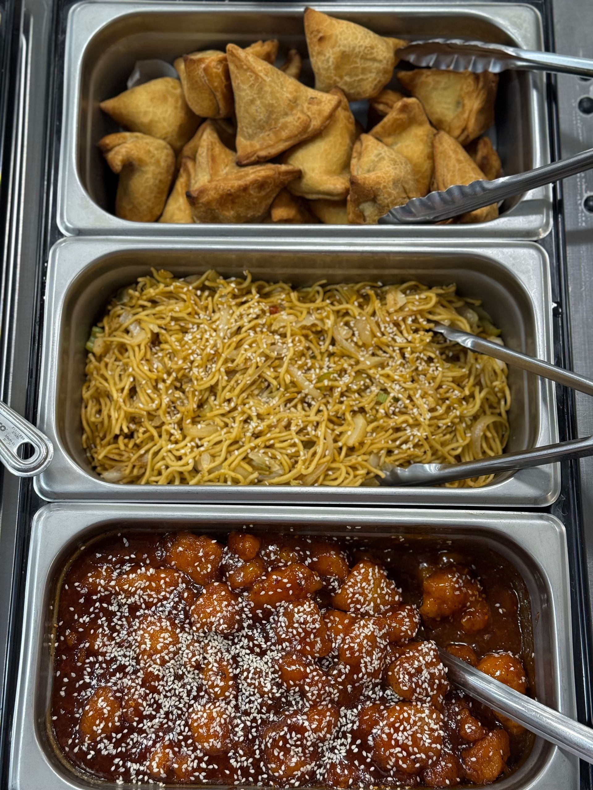 Buffet food: samosas, noodles with sesame seeds, and orange chicken.