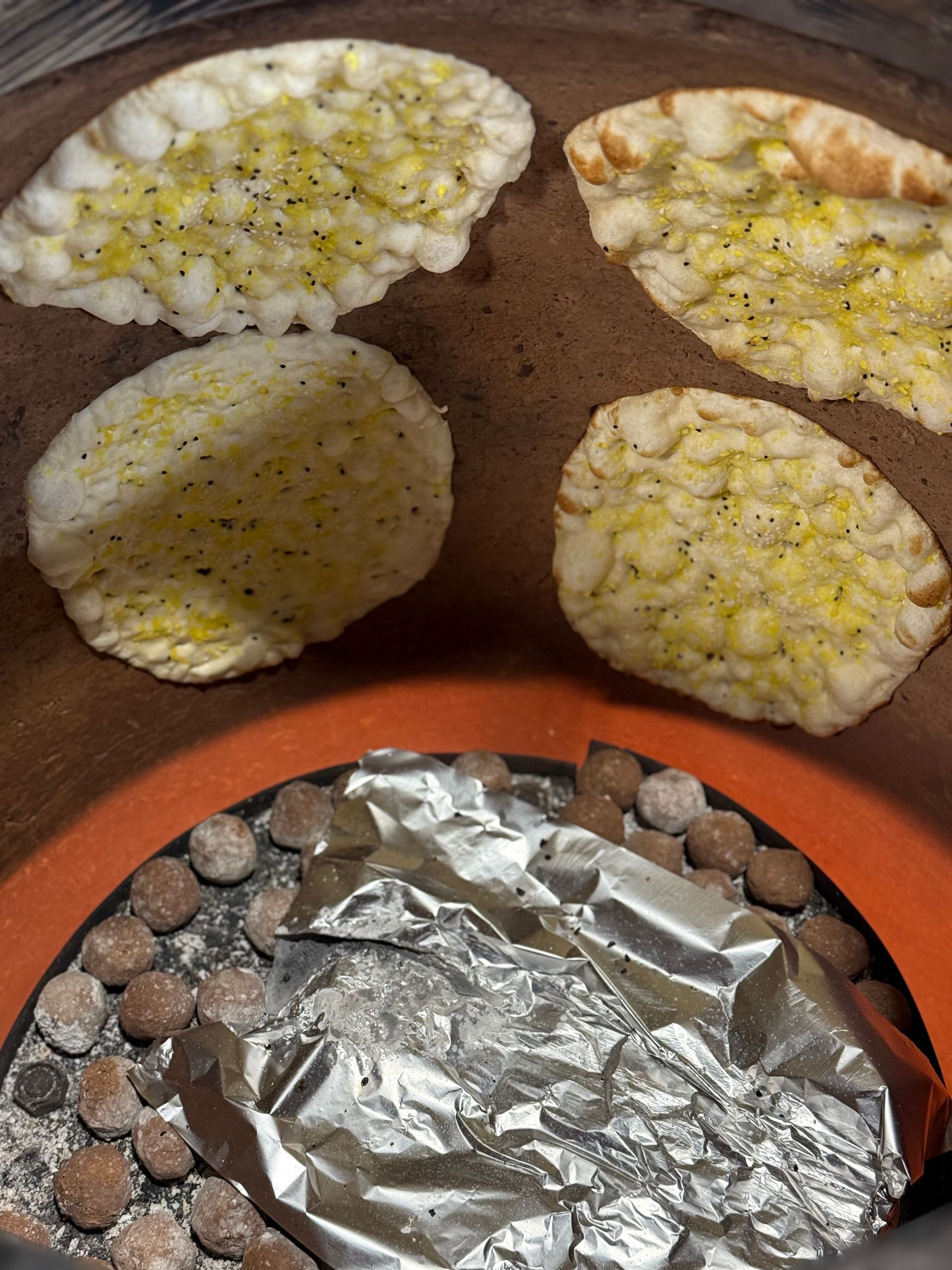 Four naan breads seasoned on a tandoor's hot surface, with charcoal below.