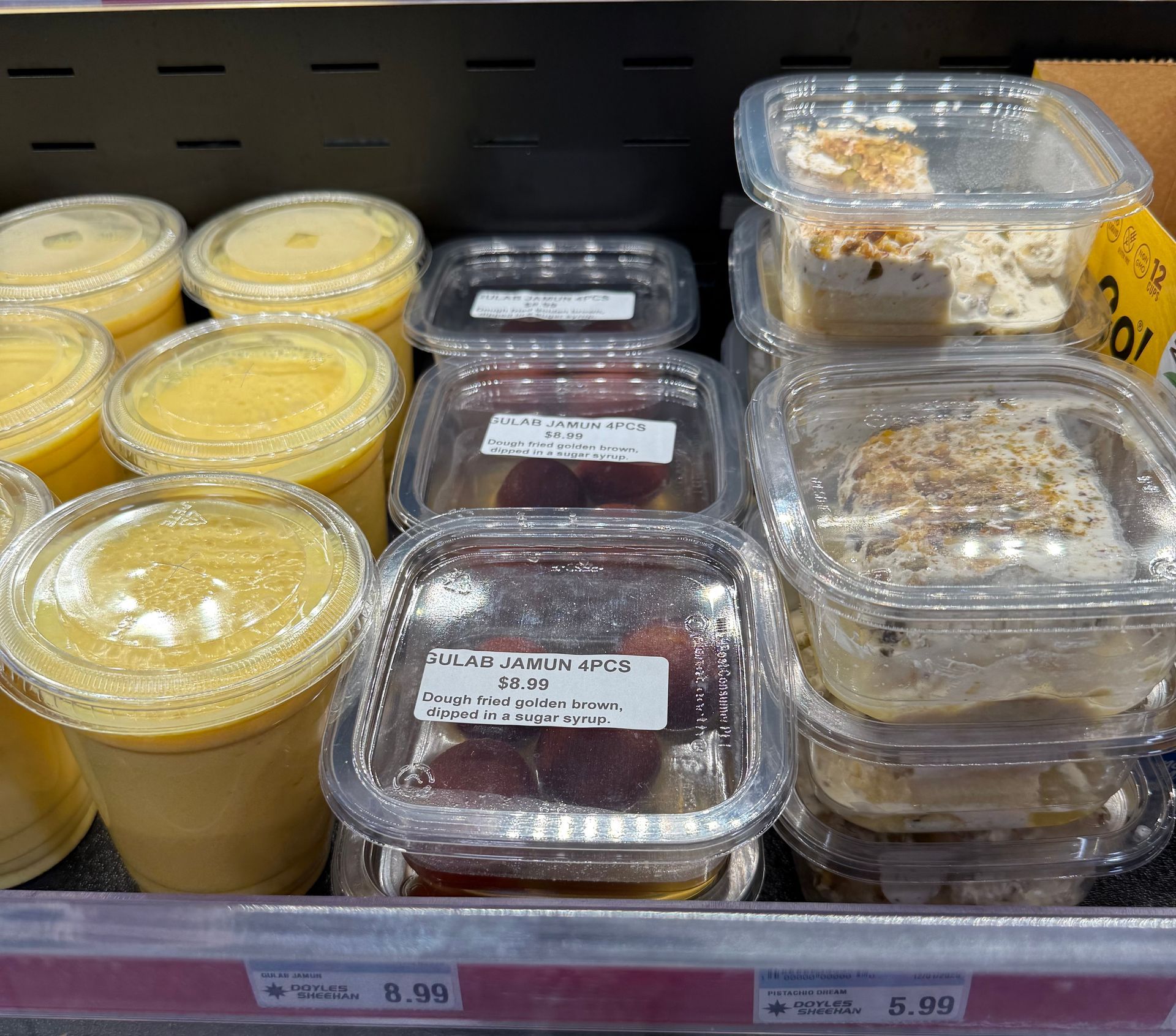 Prepared food in clear containers on a shelf; mango smoothies, meat packs, and bagels are visible.
