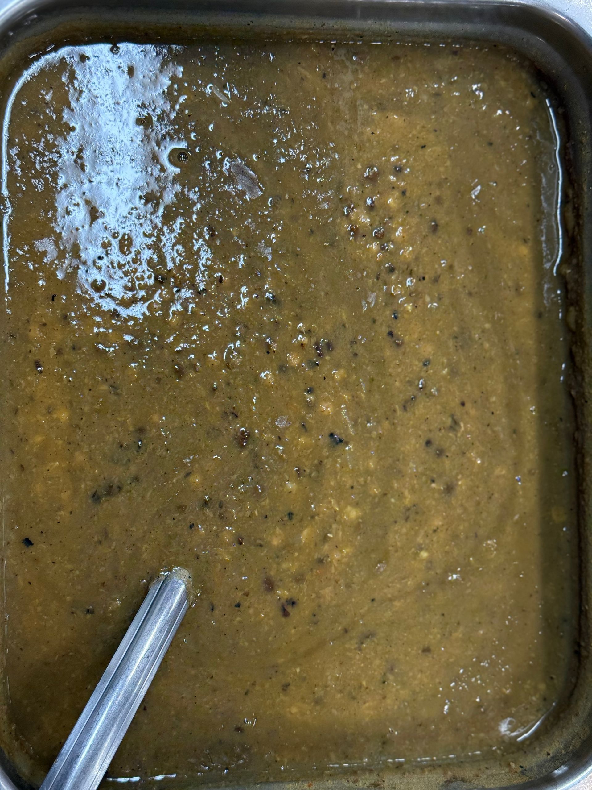 Dark green soup in a metal tray with a serving spoon.