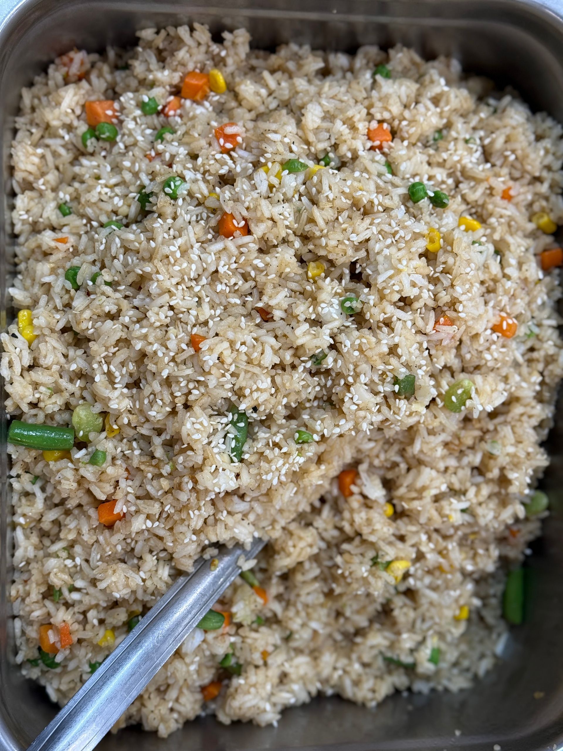 Fried rice in a metal pan, mixed with vegetables and sesame seeds.