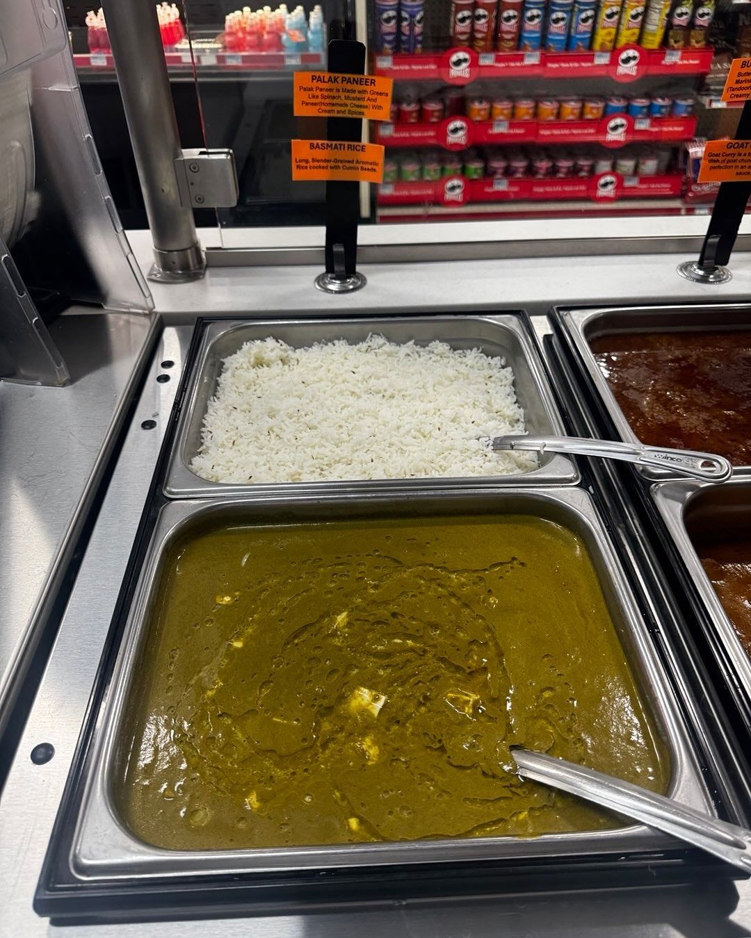 Food buffet with white rice and green curry in metal trays.