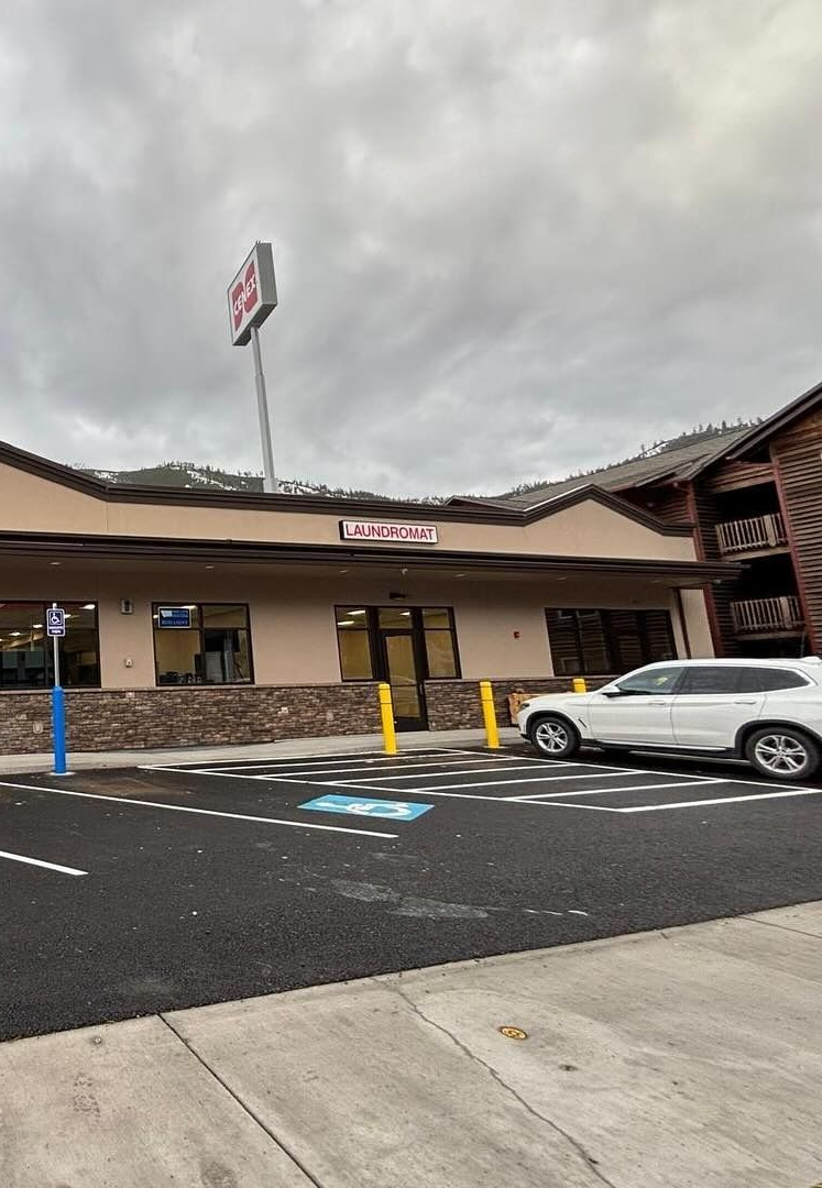 Exterior of a store with a tall sign. A white SUV is parked in front, with a cloudy sky overhead.