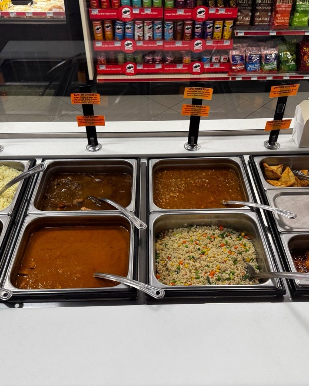 Buffet-style food containers with Indian dishes, including curry and rice, at a convenience store.
