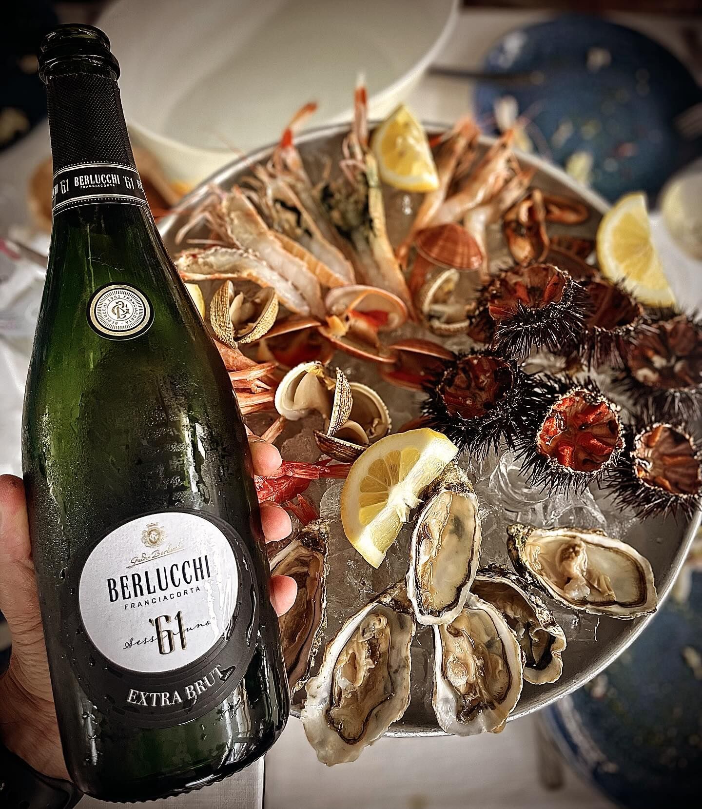 Una persona tiene in mano una bottiglia di champagne davanti a un piatto di cibo.