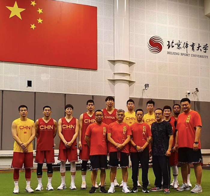 A group of basketball players are posing for a picture in front of a chinese flag