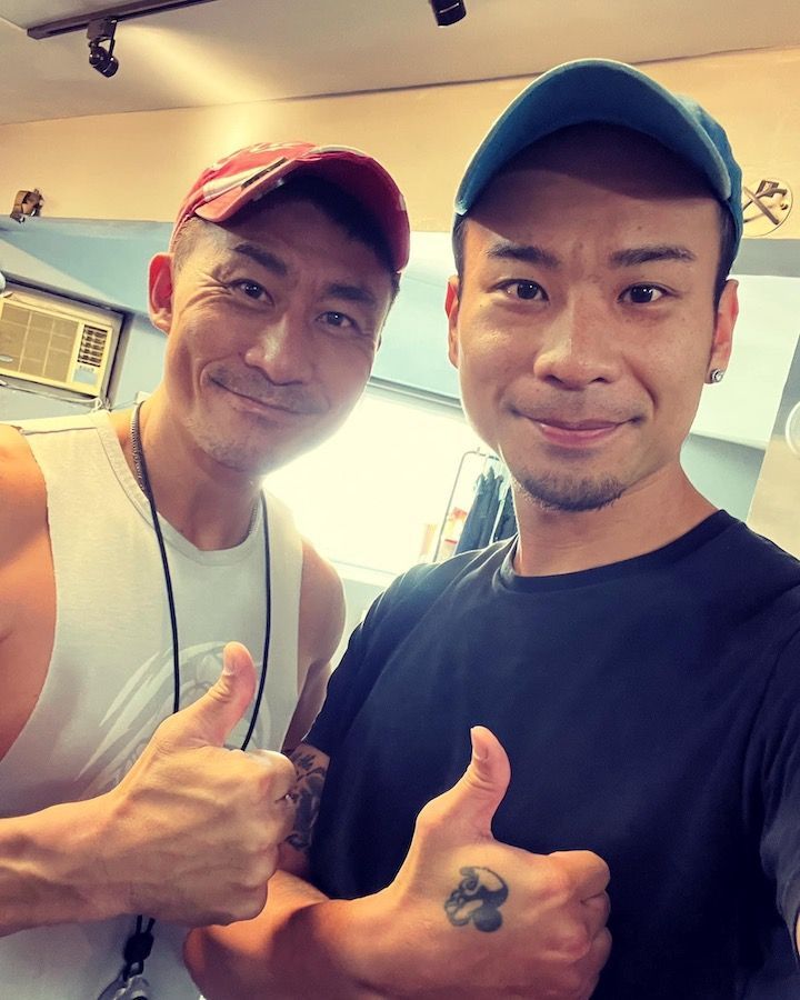 Two men are posing for a picture and one has a tattoo on his arm.