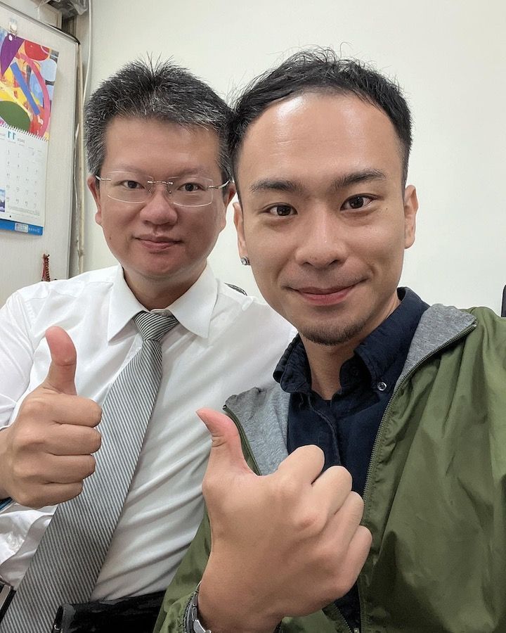Two men are posing for a picture and one of them is giving a thumbs up.