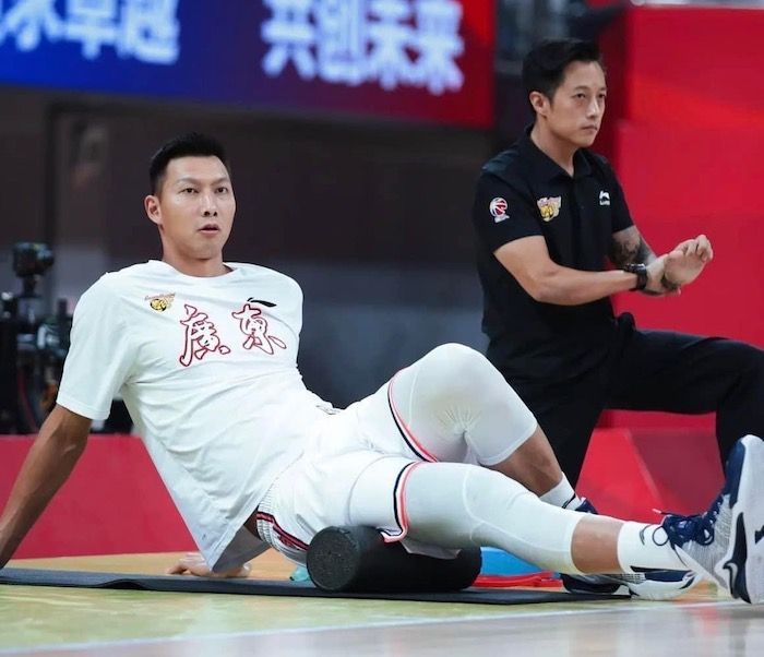 A basketball player is laying on the floor with his legs crossed