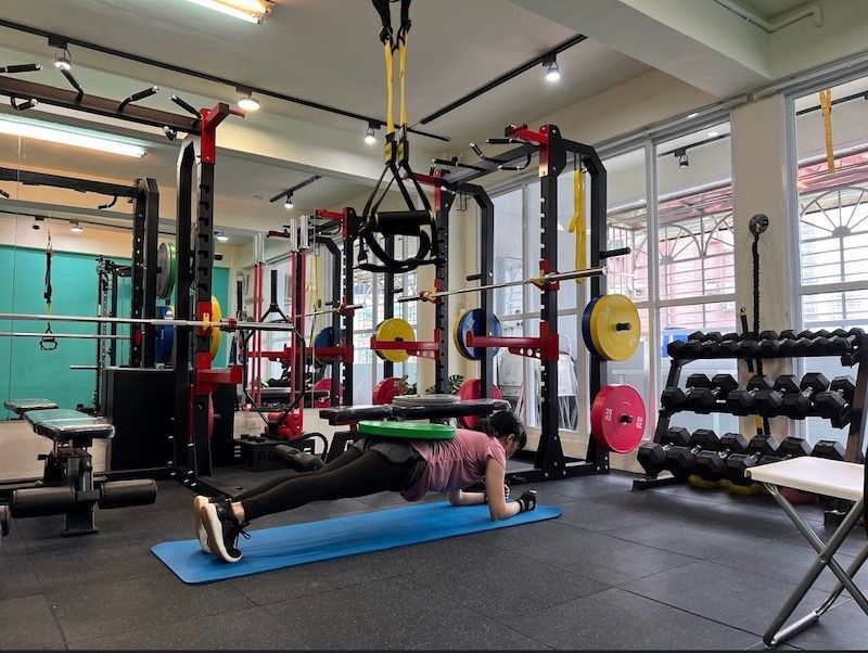 A woman is doing push ups on a blue mat in a gym.
