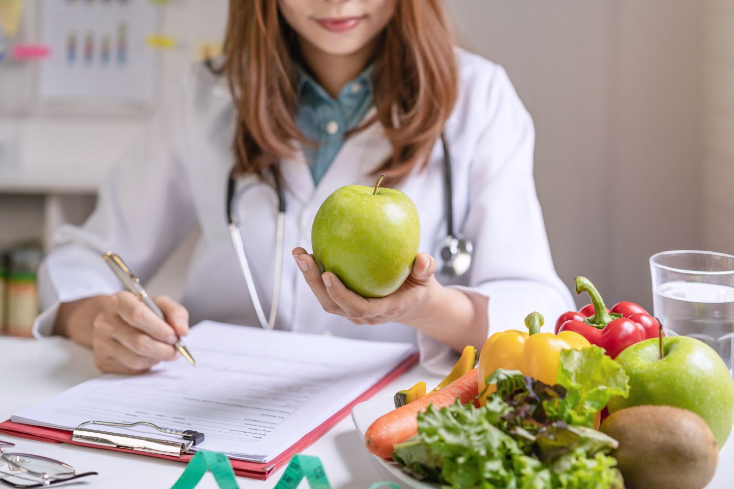 A female dietitian is holding an apple and writing on a clipboard.