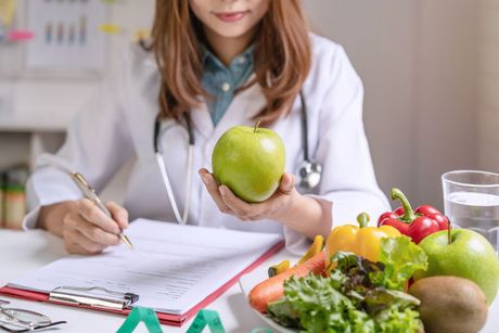 A female dietitian is holding an apple and writing on a clipboard.