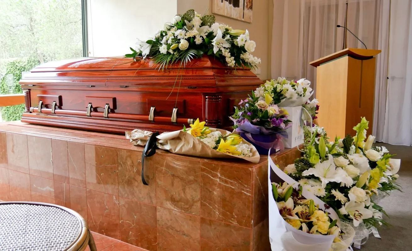 Una bara è posta in una stanza con fiori e un podio.