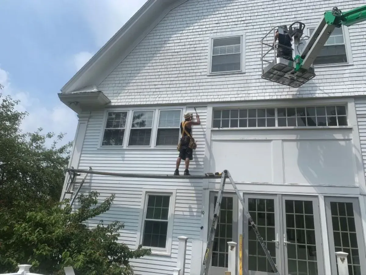A man is standing on a ladder on the side of a white house.