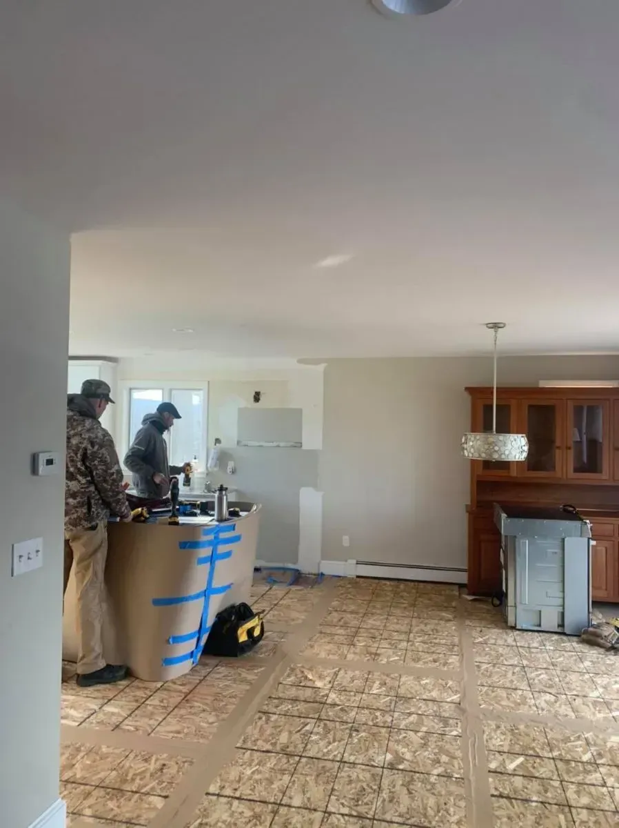 A couple of men are working on a kitchen in a house.