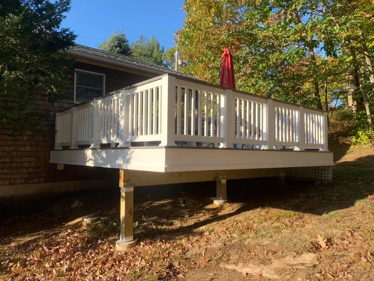 A white deck with a red umbrella on top of it is in front of a house.