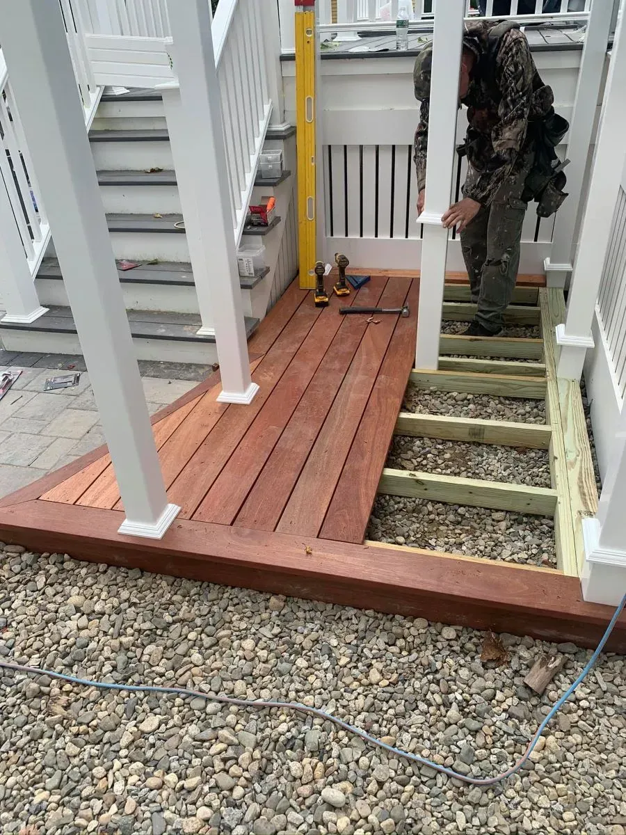 A man is working on a wooden deck next to stairs.