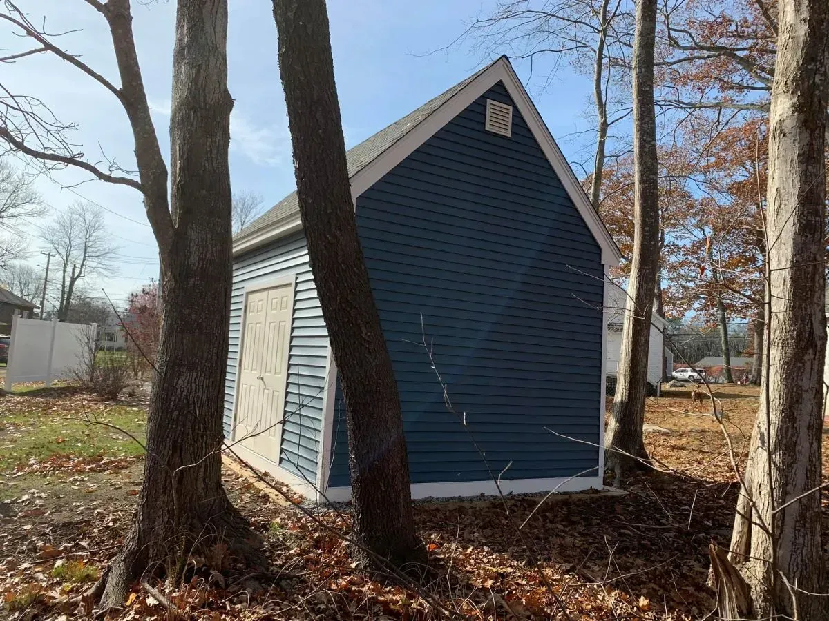 A blue shed is surrounded by trees on a sunny day