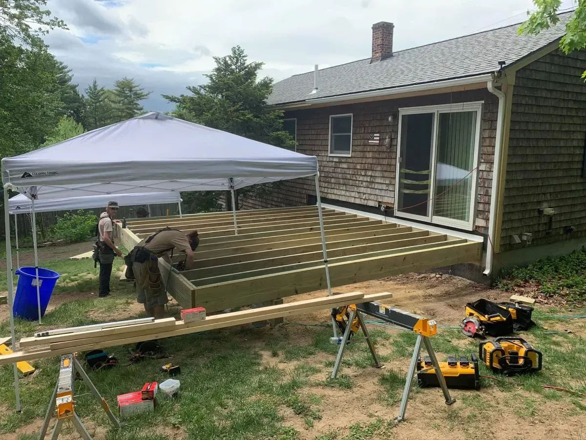 A man is working on a wooden deck in front of a house.