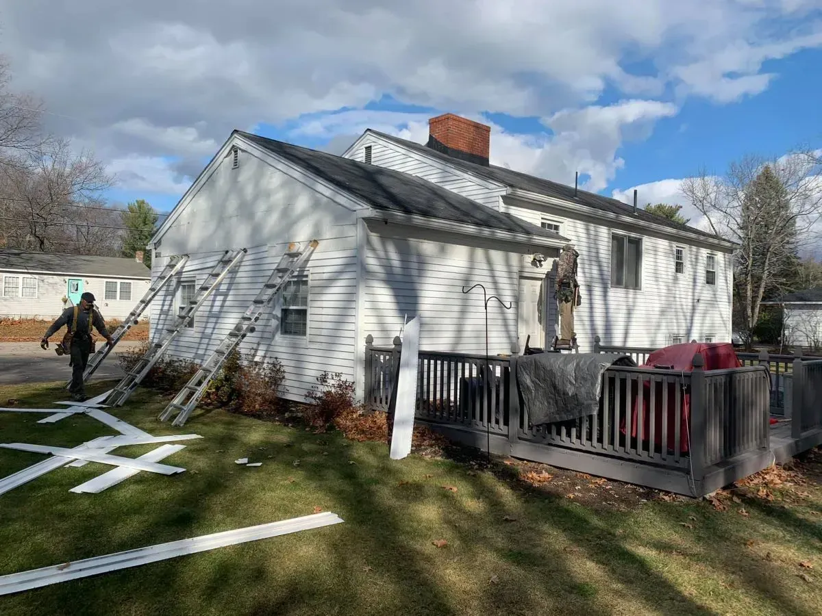 A man is standing in front of a white house with a deck.