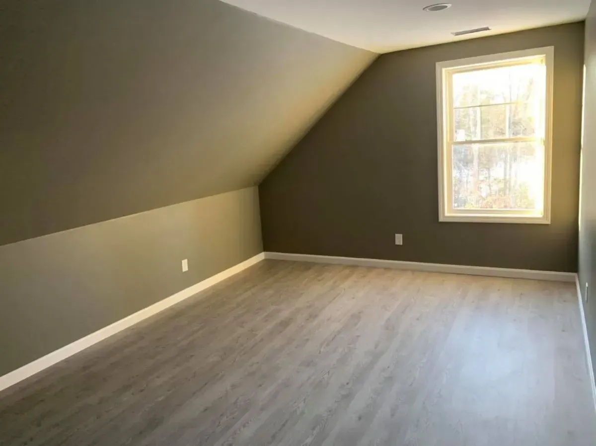 An empty room with a slanted ceiling and a window.