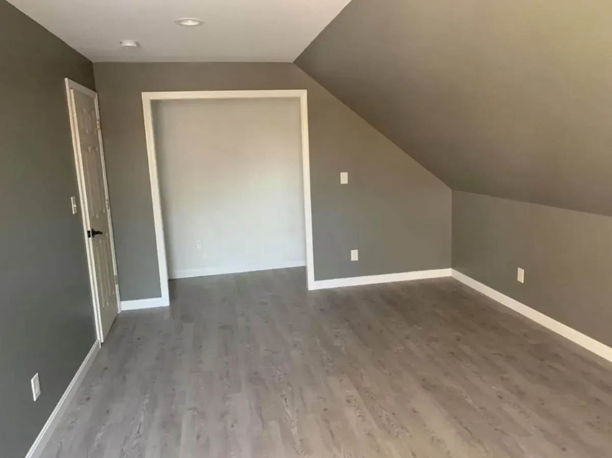 An empty room with a slanted ceiling and a closet.