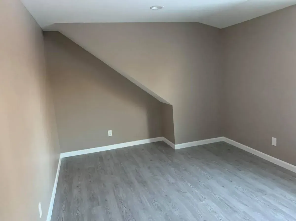 An empty room with a slanted ceiling and a wooden floor.