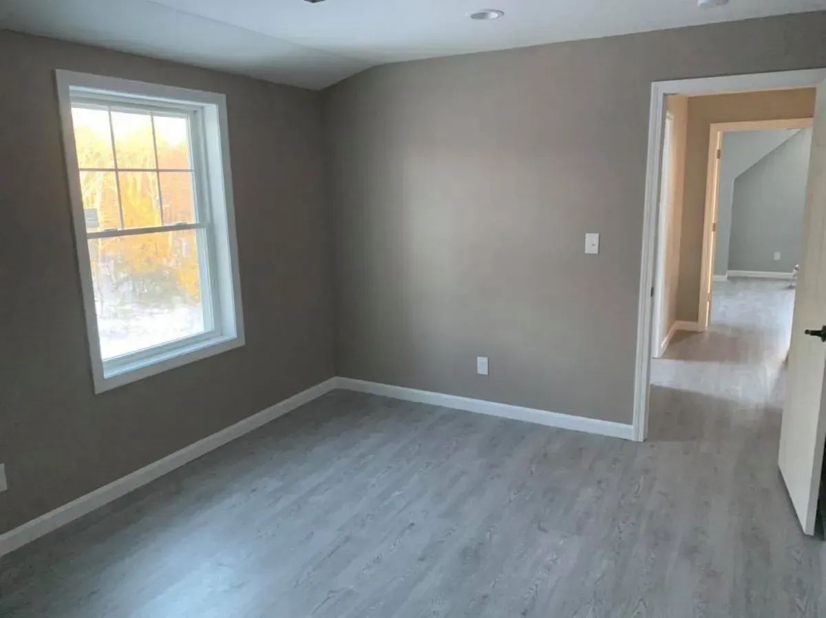 An empty room with a window and hardwood floors in a house.