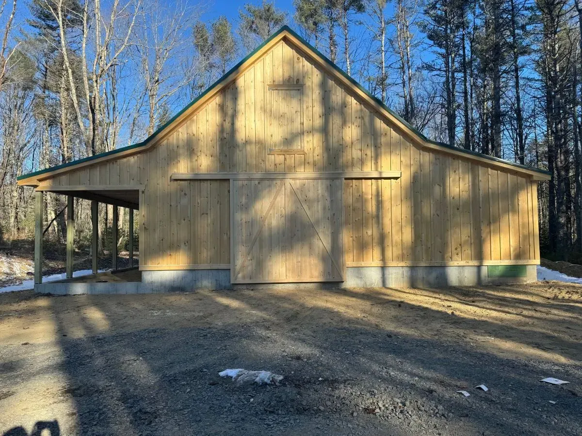 A large wooden barn is sitting in the middle of a dirt field.