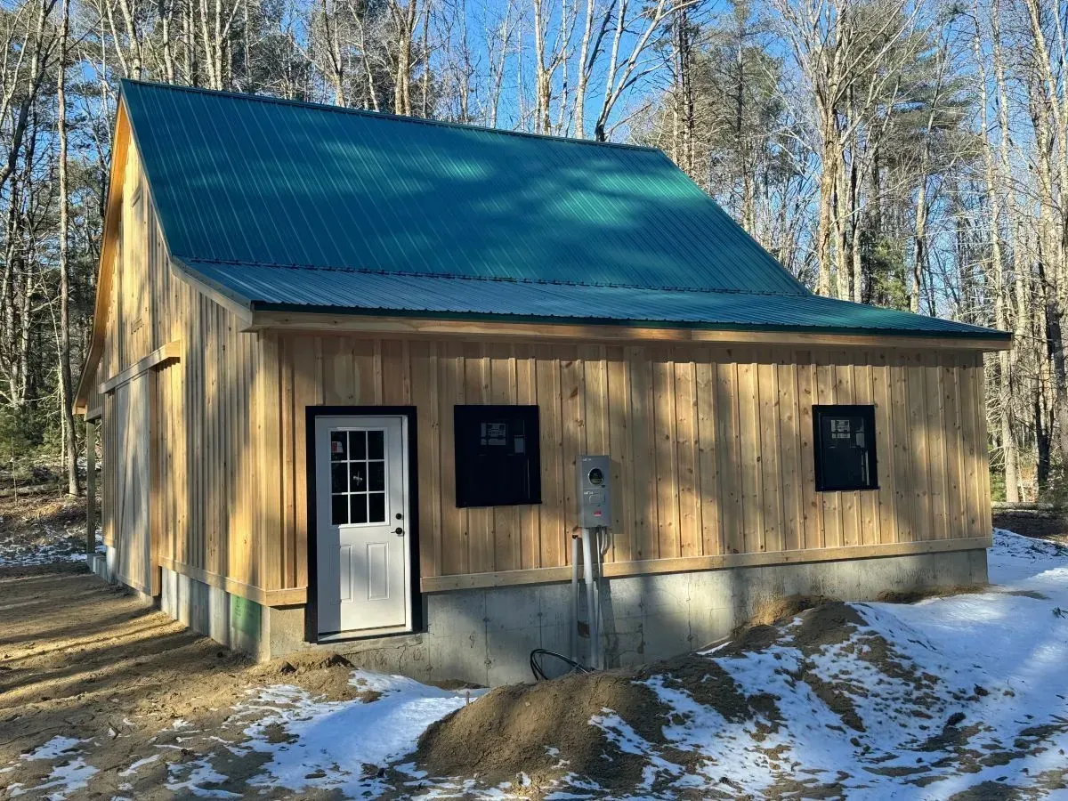 A small wooden house with a green roof is sitting in the middle of a snowy field.