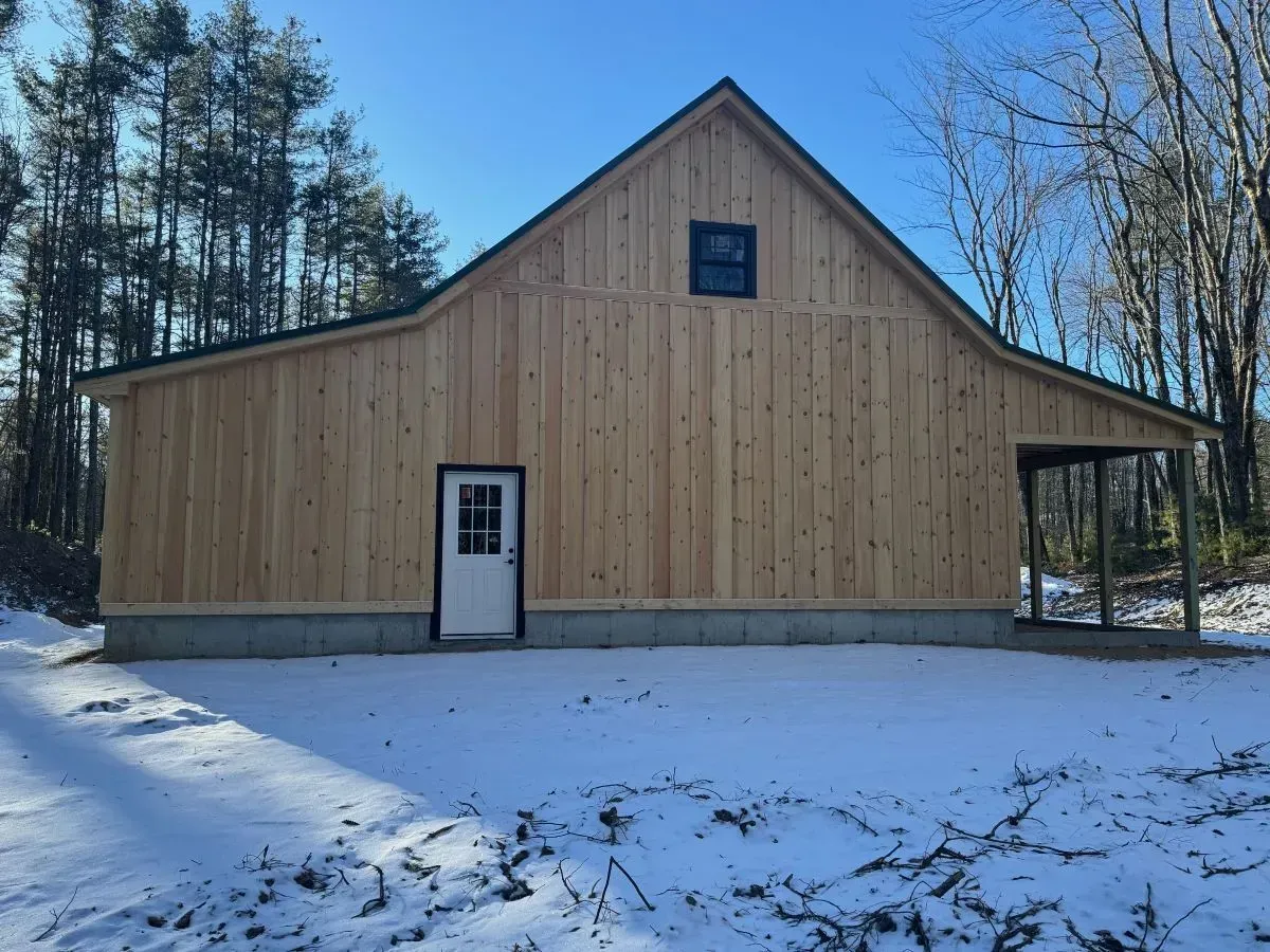 A wooden barn with a white door is surrounded by snow