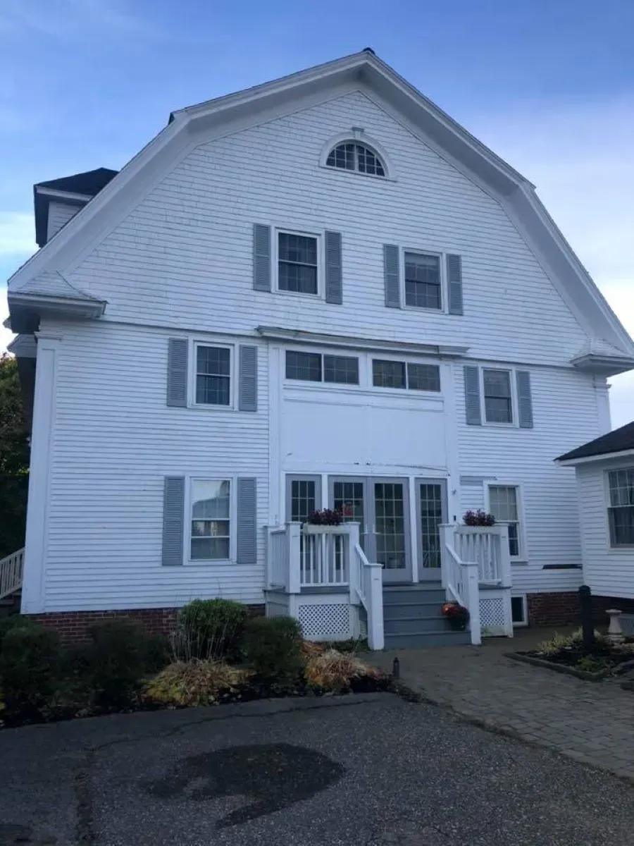 A large white house with a porch and a blue sky in the background.