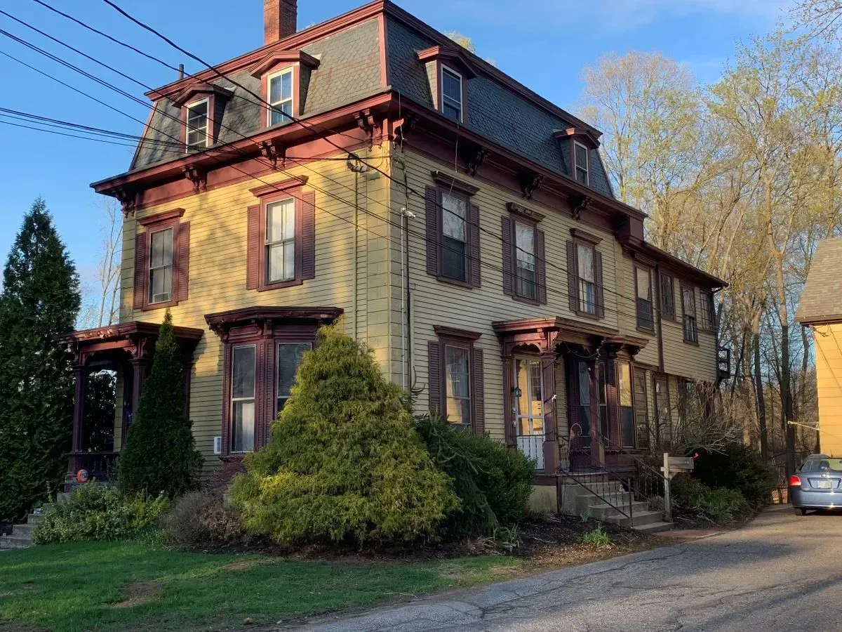 A large yellow house with red shutters is sitting on the side of a road.